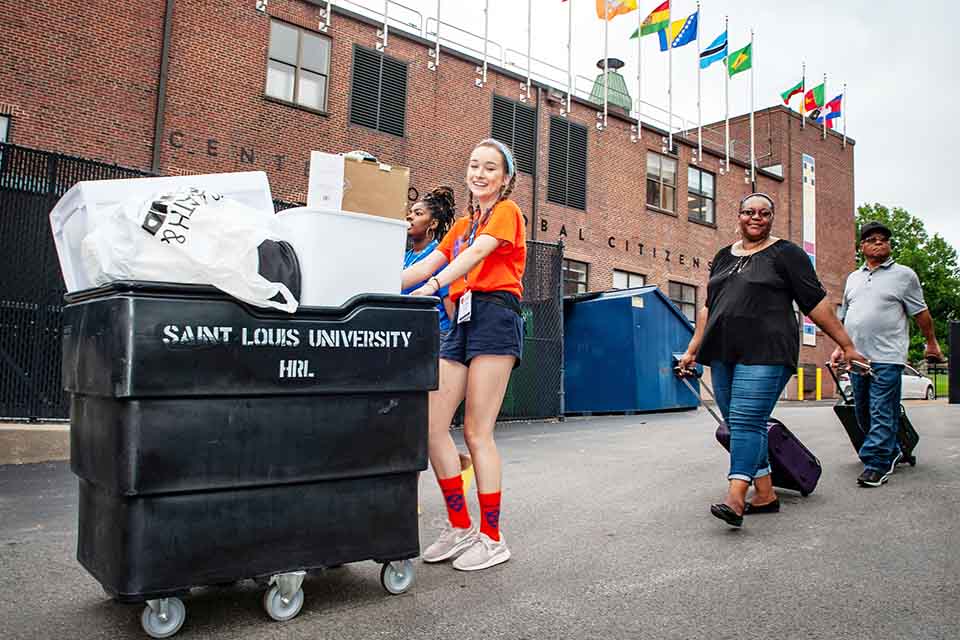 Student helping new 软妹社 family move in, pushing cart to residence hall
